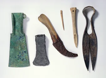 Auswahl an Werkzeugen: L-R: frühe Eisenzeit Bronzeaxt mit umgebogenen Flügeln; spätere Eisenaxt; Messer mit einem Knochenheft; Knochennadel; Knochenpfriem; Eisenschere